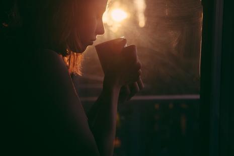 Photo of lady drinking hot drink by a window