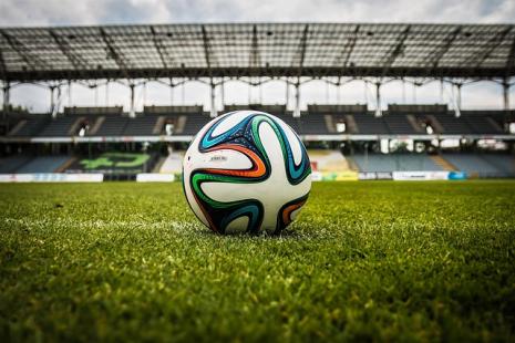 Photo of a football in the centre of a football pitch with stadium seating behind